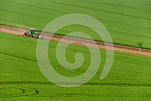 Scenic View Of Modern Farming Tractor Which Plowing Green Field. Agriculture Tractor Cultivating Wheat Field And Creating Green Ab photo