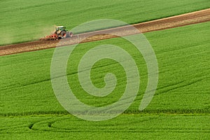 Scenic View Of Modern Farming Tractor Which Plowing Green Field. Agriculture Tractor Cultivating Wheat Field And Creating Green Ab