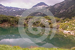 Scenic view of Okoto lake reflecting green shrubs and snowy Pirin mountain on its shore in Bulgaria