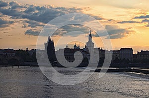 Scenic view of Old Town and Vltava River during sunrise. Buildings reflected in water. The sun hid behind the clouds