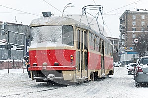 Scenic view of old vintage retro tram driving snowy Kiev city streets with traffic at heavy snowfall blizzard on cold