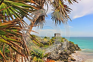 Scenic view through palm trees leaves to ancient Mayan ruins of God of Winds Temple