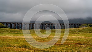 Scenic view of a railway bridge on a cloudy day, with grassy landscape in the foreground