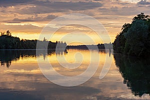 Scenic view of a reflective river with green shoreline trees at sunrise