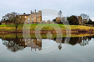 Scenic view of Ripley Castle reflecting in a lake against a cloudy sky in England.