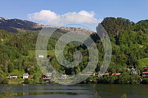 Scenic view of a river and green mountain forests with houses at Narrow Fjord in Vestland, Norway