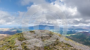 A scenic view of a rocky mountain summit with valley and mountain range in the background under a stormy grey cloudy sky