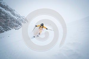 Scenic view of a skier with a yellow ski suit, skiing down a snowy slope