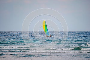 Scenic view at small catamaran with yellow green blue sail sailing in sea. Team of unrecognizable people enjoy together tropical