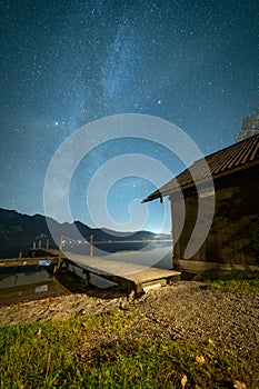 Scenic view of a starry night over a calm lake, wooden dock, and cabin