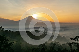 Scenic view of sunrise behind Merapi volcano, misty jungle and Borobudur temple in Indonesia photo