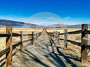Scenic view of a trail with railing in a field leading to a blue lake in mountains on a sunny day