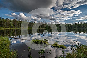 Scenic view of a tranquil lake reflecting the green trees and cloudy sky.