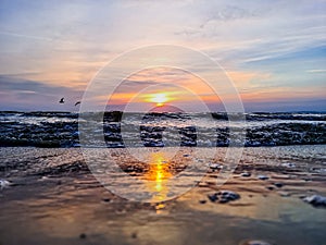 Scenic view of a wet sandy beach against sea waves reflecting sunset