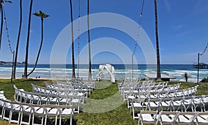 Scenic view of white chairs in a row on green grass ready for a wedding ceremony on the beach