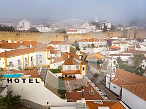 Scenic view of white houses red tiled roofs, and castle from wall of fortress with clouds. Obidos village, Portugal.