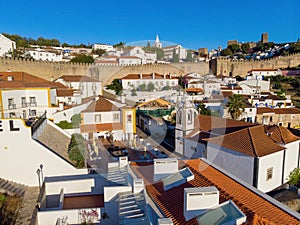 Scenic view of white houses red tiled roofs, and castle from wall of fortress. Obidos village, Portugal.