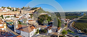 Scenic view of white houses red tiled roofs, and vineyard castle from wall of fortress. Obidos village, Portugal.