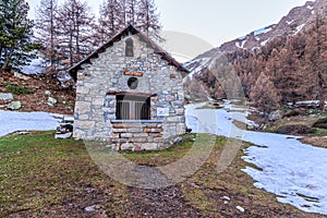 A scenic view of a winter landscape in the mountains with a chapel and some pine trees under a majestic blue sky