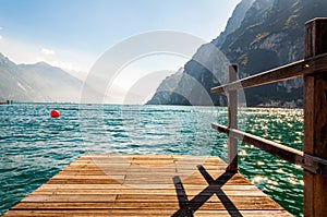 Scenic view on wooden planks pier with railings built on northern shore of beautiful Garda lake in Lombardy, Italy surrounded by