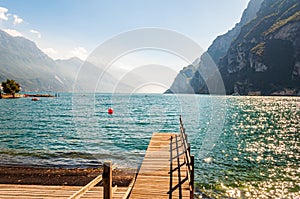 Scenic view on wooden planks pier with railings built on northern shore of beautiful Garda lake in Lombardy, Italy surrounded by