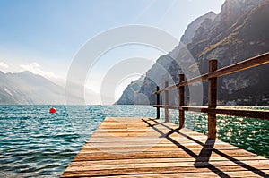 Scenic view on wooden planks pier with railings built on northern shore of beautiful Garda lake in Lombardy, Italy surrounded by