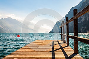 Scenic view on wooden planks pier with railings built on northern shore of beautiful Garda lake in Lombardy, Italy surrounded by