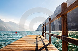 Scenic view on wooden planks pier with railings built on northern shore of beautiful Garda lake in Lombardy, Italy surrounded by