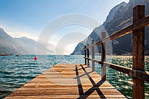 Scenic view on wooden planks pier with railings built on northern shore of beautiful Garda lake in Lombardy, Italy surrounded by