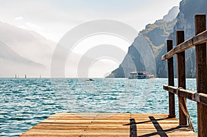 Scenic view on wooden planks pier with railings built on northern shore of beautiful Garda lake in Lombardy, Italy surrounded by