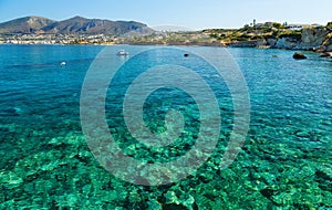 Scenic views of the seabed with green stones, a city on the shore and a small boat in bay of island Crete, Greece.