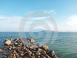 Scenic White Sand Beach with Wavy Water and Clear Blue Sky Background, Beautiful Seashore View with Mountains and stones in Summer