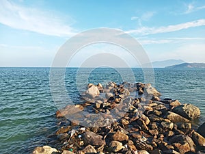 Scenic White Sand Beach with Wavy Water and Clear Blue Sky Background, Beautiful Seashore View with Mountains and stones in Summer