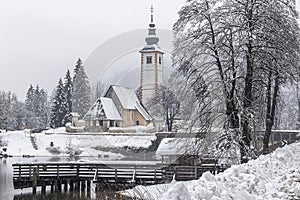 Scenic winter landscape of Bohinj lake in Gorenjska with old bridge and Church