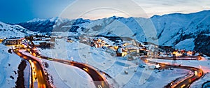 Scenic winter landscape in Gudauri with caucasus mountains background and holiday hotels and road with cars on evening