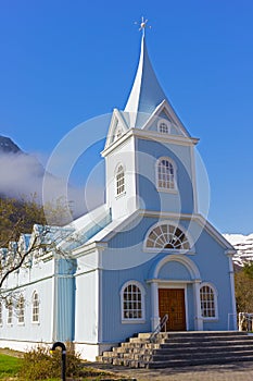 Scenic wooden church painted in blue color against mountainous landscape in Northern Iceland.