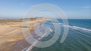 A scenics aerial view of a sandy beach with hill cliff in the background along a beautiful choppy blue see under a majestic blue