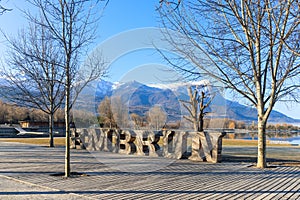 A scenics view of the Embrun, France lake with wooden sign, snowy mountains range in the background under a majestic blue sky