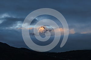 A scenics view of majestic snowy mountain summit engulfed in white altitude clouds with reflecting sun, Hautes-alpes, France