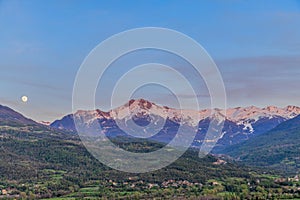 A scenics view of majestic snowy mountain summit (Les Orres) at dawn with a full moon, Hautes-alpes, France