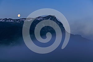 A scenics view of majestic snowy mountain summit (Pic de Morgon) at dawn with a full moon, Hautes-alpes, France