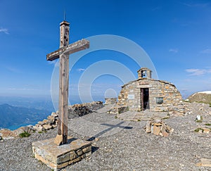 A scenics view of a mountain summit with a chapel and cross under a majestic blue sky and some white clouds