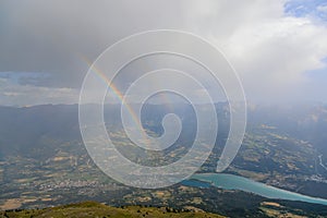 A scenics view of a mountain summit with a majestic double rainbow and Embrun, Hautes-alpes, France in the background under a