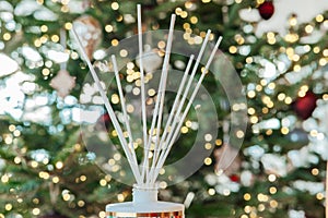 Scent of Christmas. Diffuser with sticks with aroma of vanilla, oranges and cinnamon on Christmas shining tree