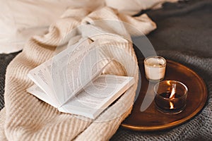 Scented burning candle with open paper book in bed close up