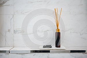 Scented diffuser stick in black glass bottle against white marble wall background