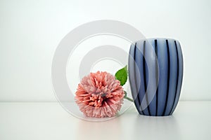 Scented gray striped candle on a white surface. Pink terry artificial flower on a white background. Still life, interior