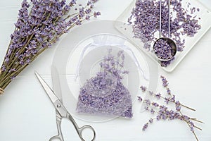 Scented sachet with dried lavender flowers and scissors on white wooden table, flat lay