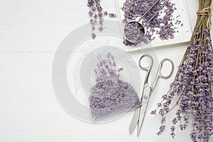Scented sachet with dried lavender flowers and scissors on white wooden table, flat lay. Space for text