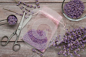 Scented sachet with dried lavender flowers and scissors on wooden table, flat lay